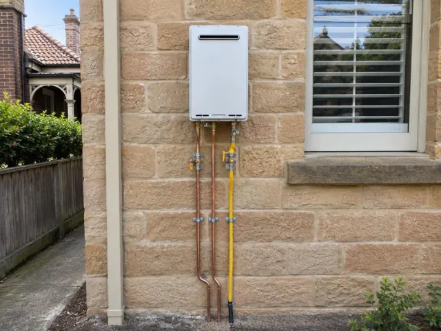 Wall-mounted hot water unit with copper and gas pipework on a sandstone exterior wall in Randwick