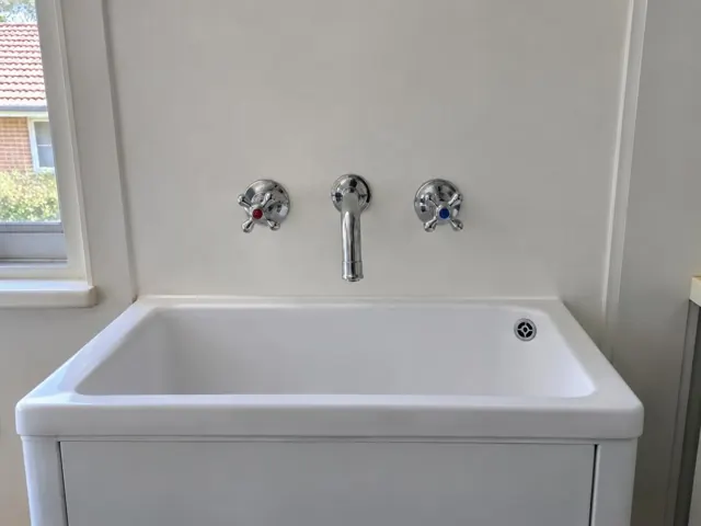 White laundry sink with a new chrome tap and dry bench against a pale wall in Coogee